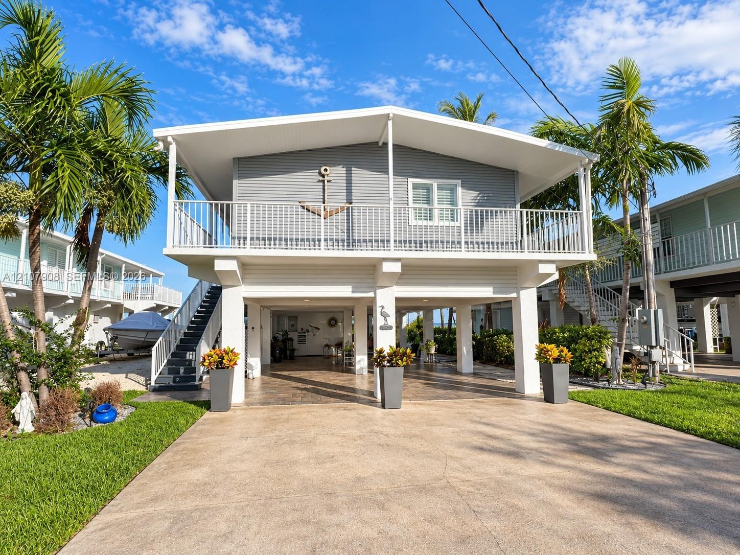 Elevated coastal home featuring horizontal siding, a full-width balcony with metal railings, a covered ground-level parking area, and concrete drive