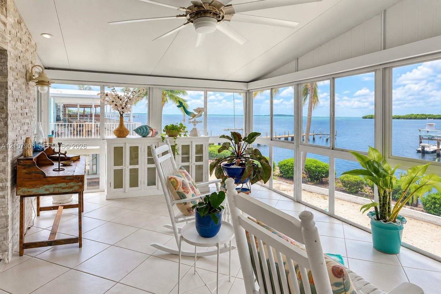 Enclosed sunroom featuring floor-to-ceiling screen panels, white tile flooring, natural stone-accent wall, and a ceiling fan