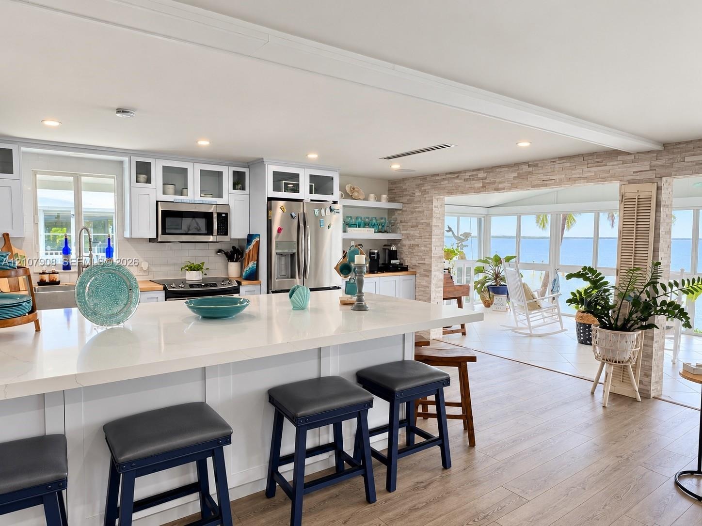 Kitchen featuring a white quartz island countertop, stainless steel appliances, white cabinetry with glass-front uppers, stacked stone accent wall, an