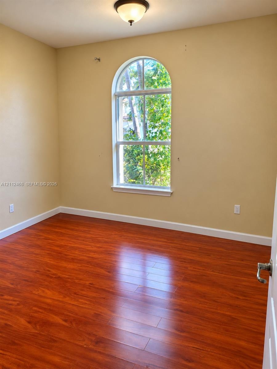 Room featuring arched window, wood-finish flooring, and overhead flush-mount lighting