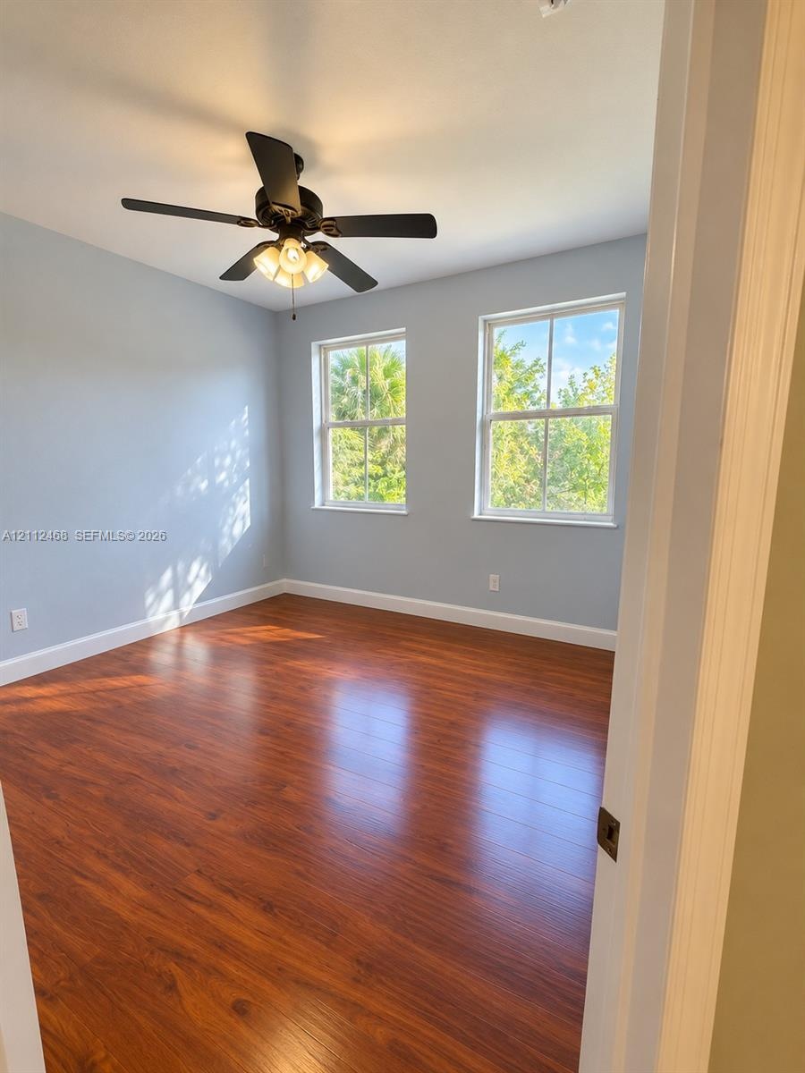 Room featuring wood-finish flooring, dual windows with muntins, and a ceiling fan with integrated lighting