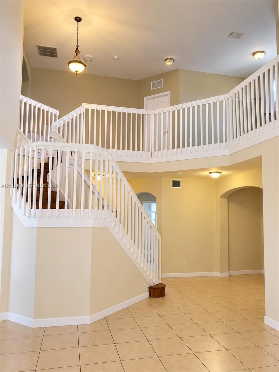 Two-story foyer featuring a vaulted ceiling, prominent staircase with a white balustrade, tile flooring, arched doorways, and a traditional pendant li