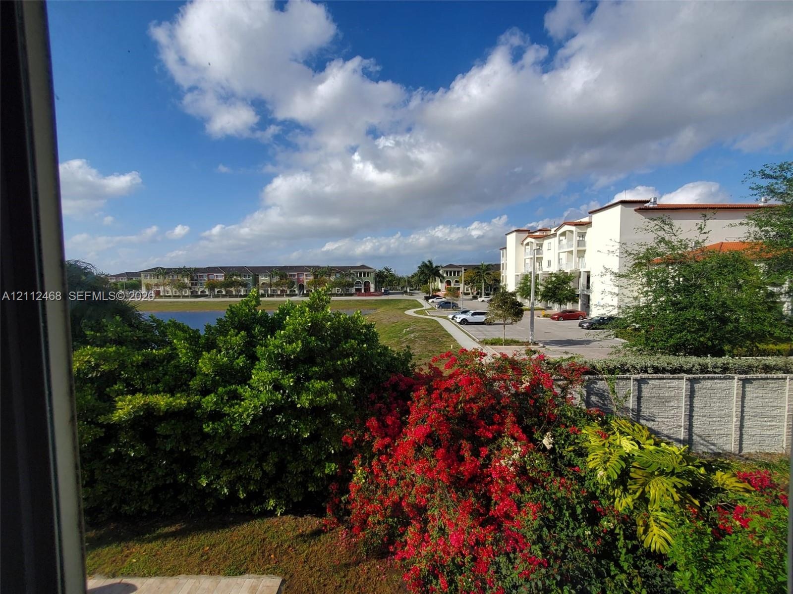 Exterior grounds featuring a retention pond, mature landscaping with flowering shrubs, paved parking area, and decorative concrete perimeter wall