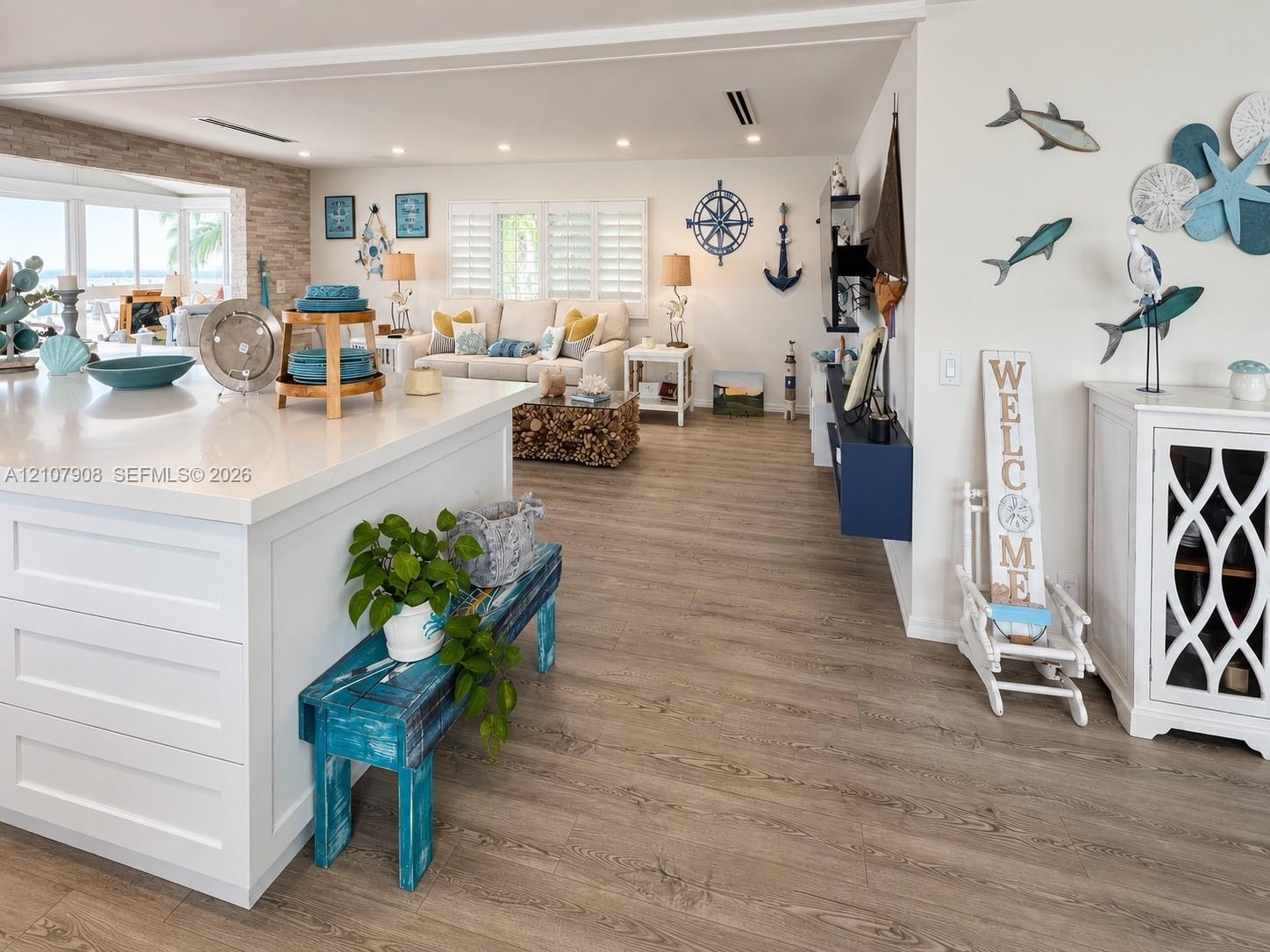 Kitchen featuring a large central island with white cabinetry and solid-surface countertops, wood-finish flooring, recessed lighting, plantation shutt