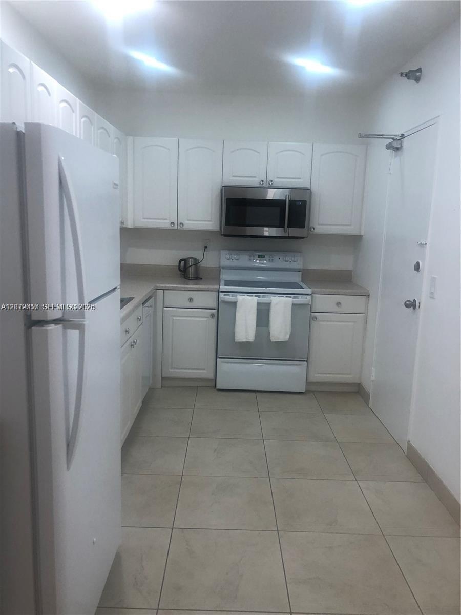 Kitchen featuring white cabinetry, solid-surface countertops, tile flooring, and stainless steel microwave and oven appliances
