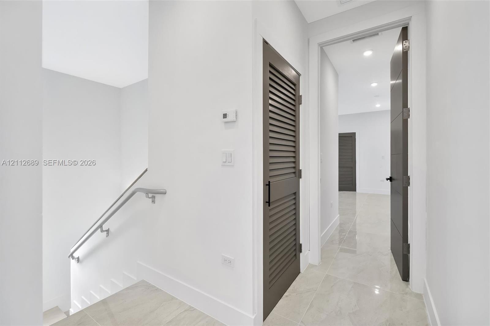 Neutral-toned tile flooring, louvered-style closet door, solid-core interior doors with matte black hardware, and recessed ceiling lighting