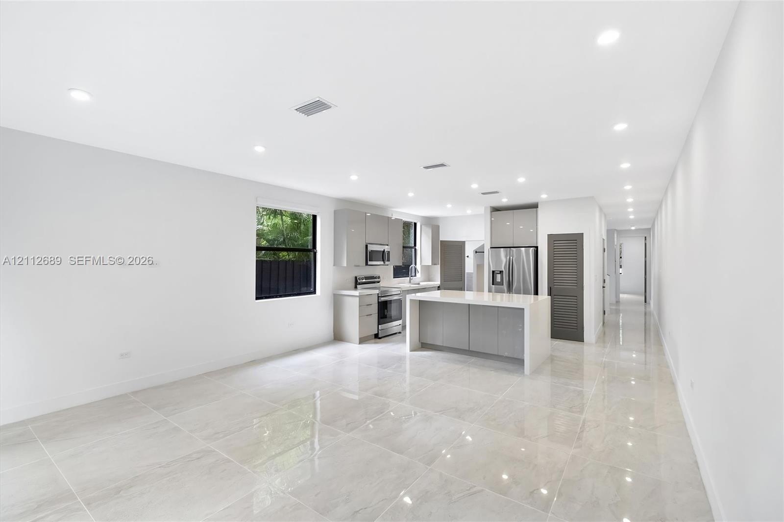 Kitchen featuring high-gloss cabinetry, stone-finish countertops, stainless steel appliances, a central island, and large-format porcelain tile floori