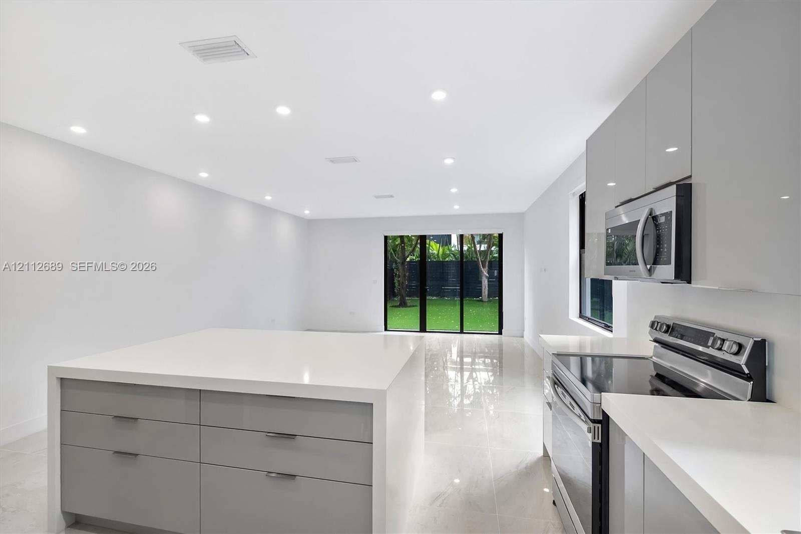 Modern kitchen featuring high-gloss cabinetry, stone-surface waterfall island, stainless steel appliances, recessed ceiling lighting, and polished til