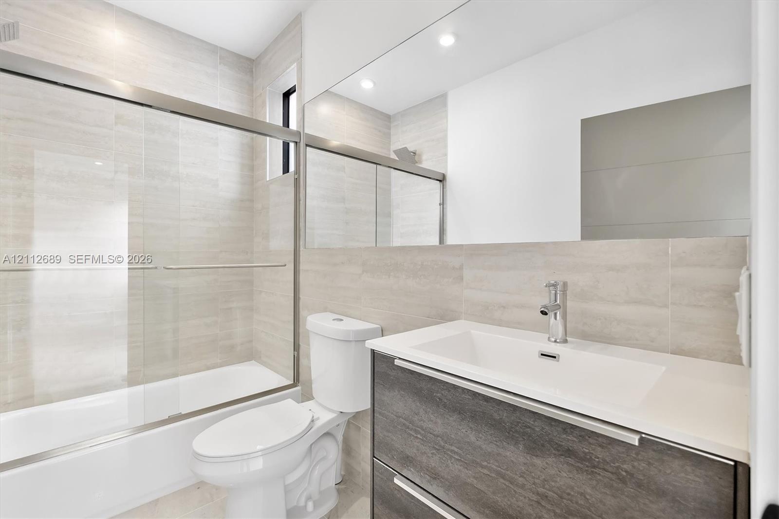 Bathroom featuring a wall-to-wall mirror, modern floating vanity with a stone-top integrated sink, floor-to-ceiling tile surround, and a glass-enclose