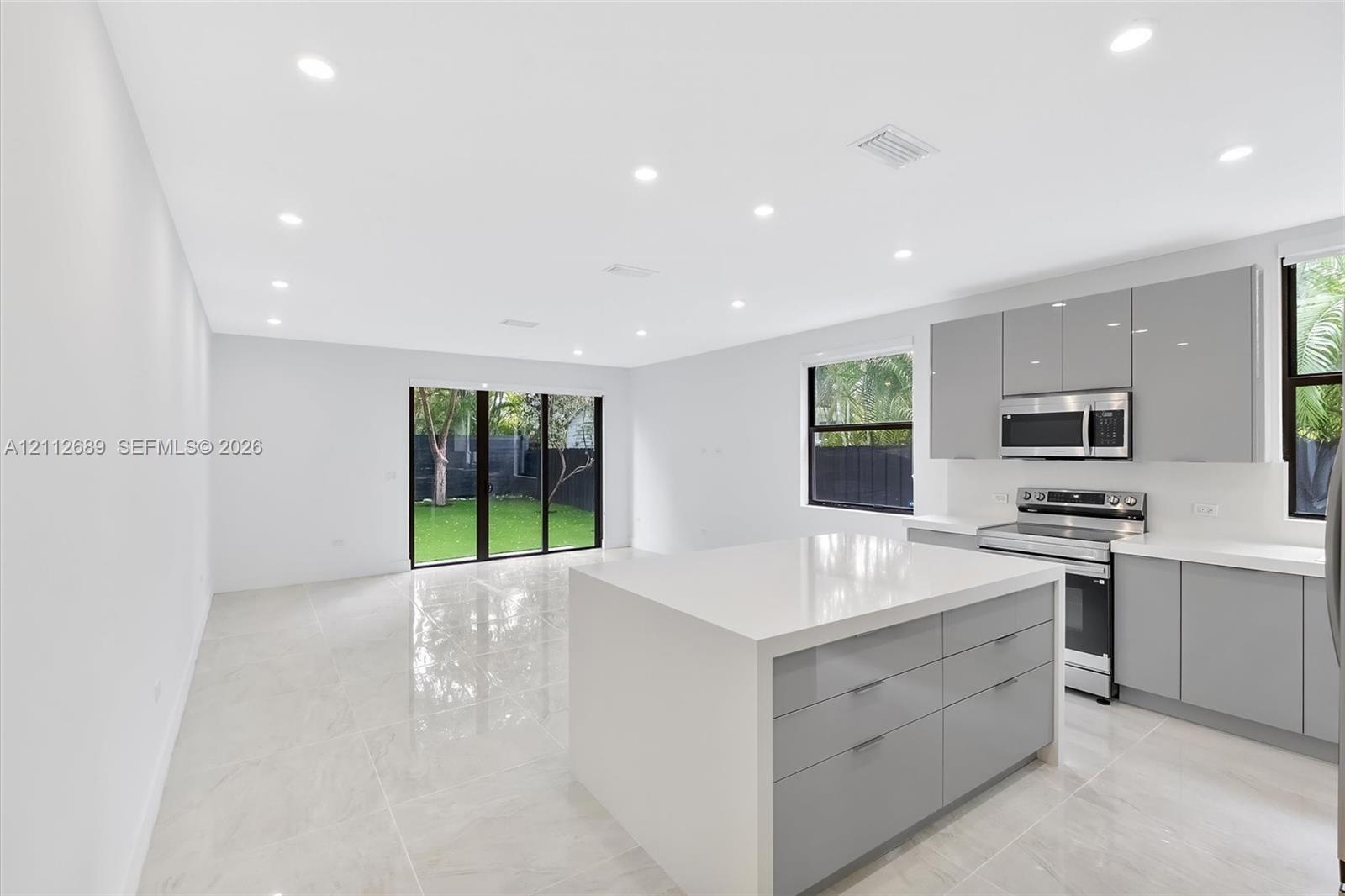 Open-concept kitchen featuring high-gloss cabinetry, a central island with a solid surface countertop, stainless steel appliances, recessed lighting, 