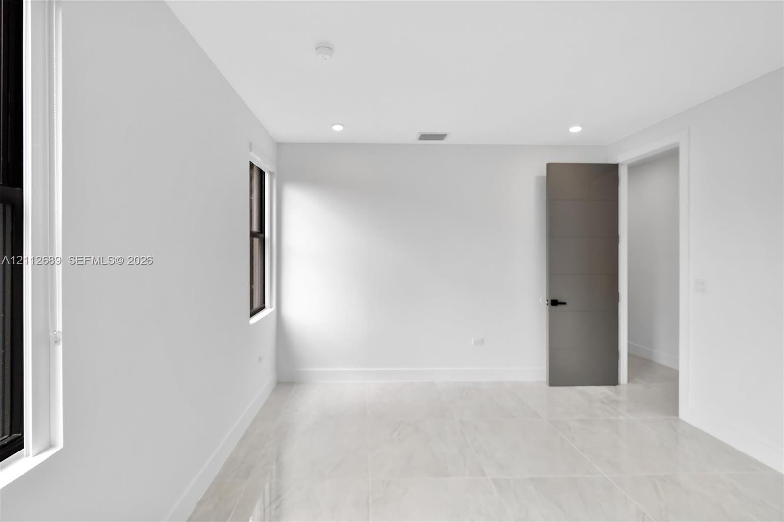 Interior space featuring large-format stone-finish tile flooring, neutral walls, recessed LED lighting, and a multi-panel door with matte black hardwa