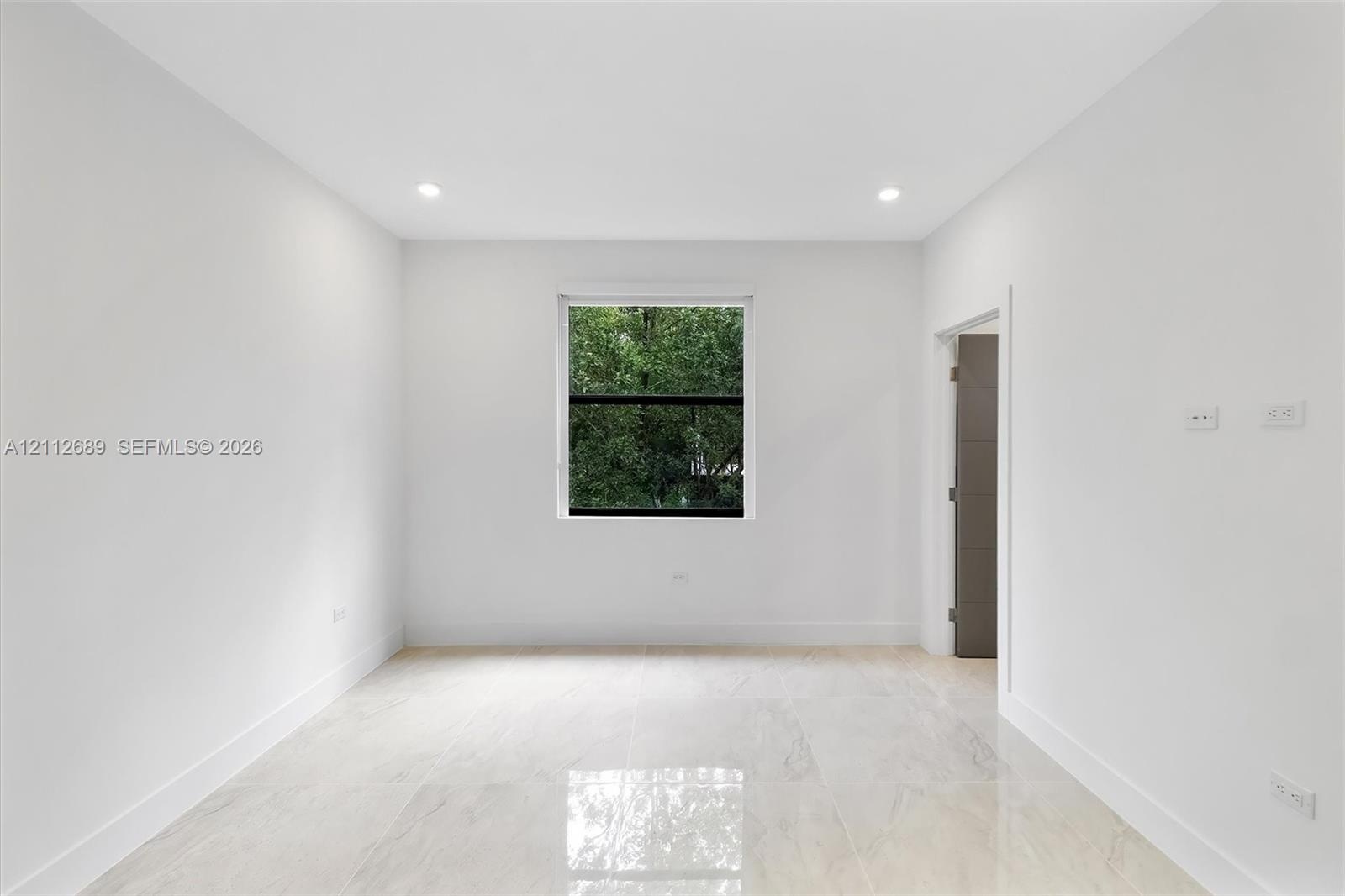 Interior space featuring large-format polished tile flooring, recessed lighting, neutral wall paint, and a single window with exterior greenery