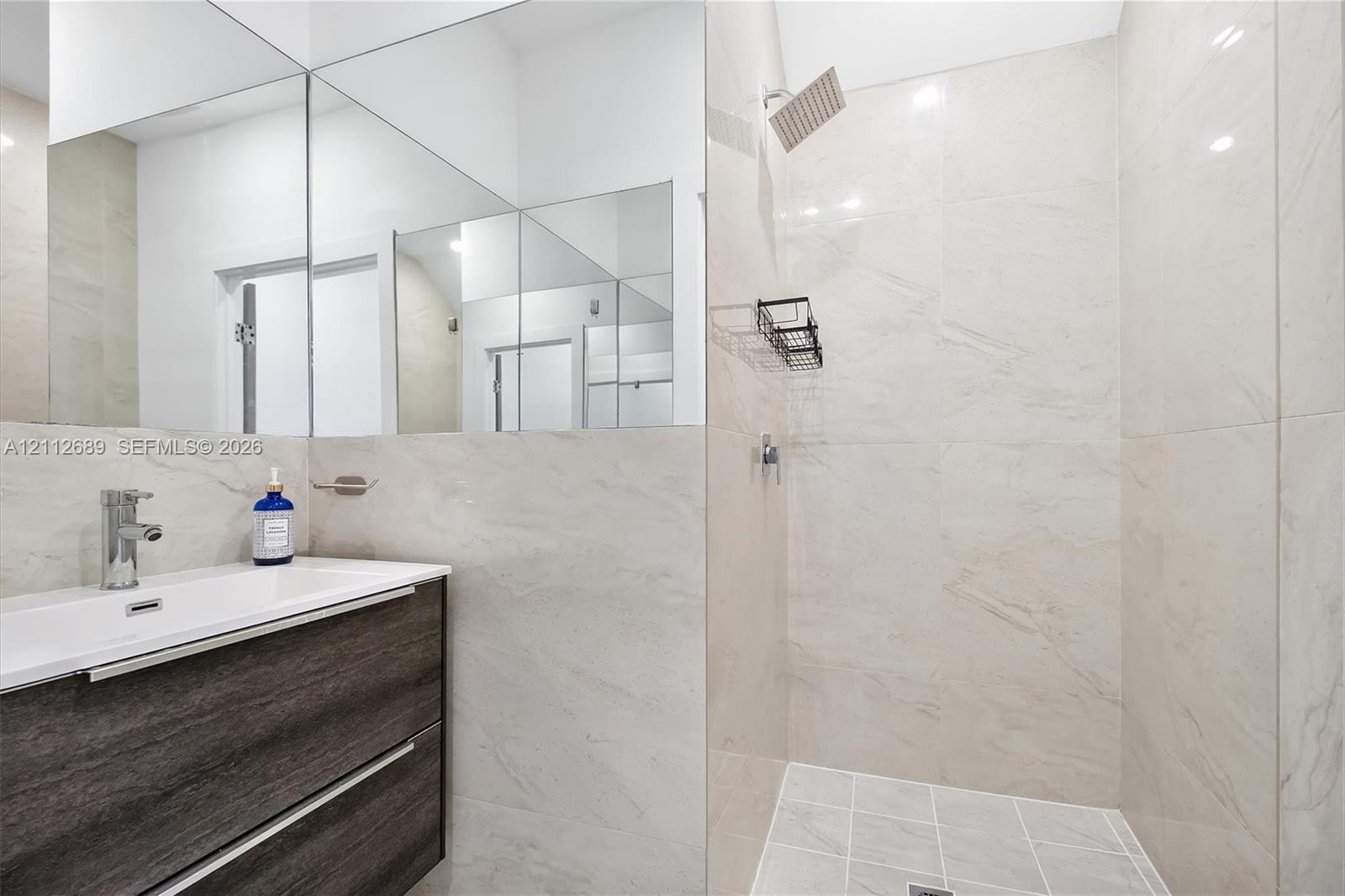 Modern floating vanity with a dark wood-finish exterior, integrated rectangular sink, wall-spanning mirror, and a walk-in shower featuring large-forma