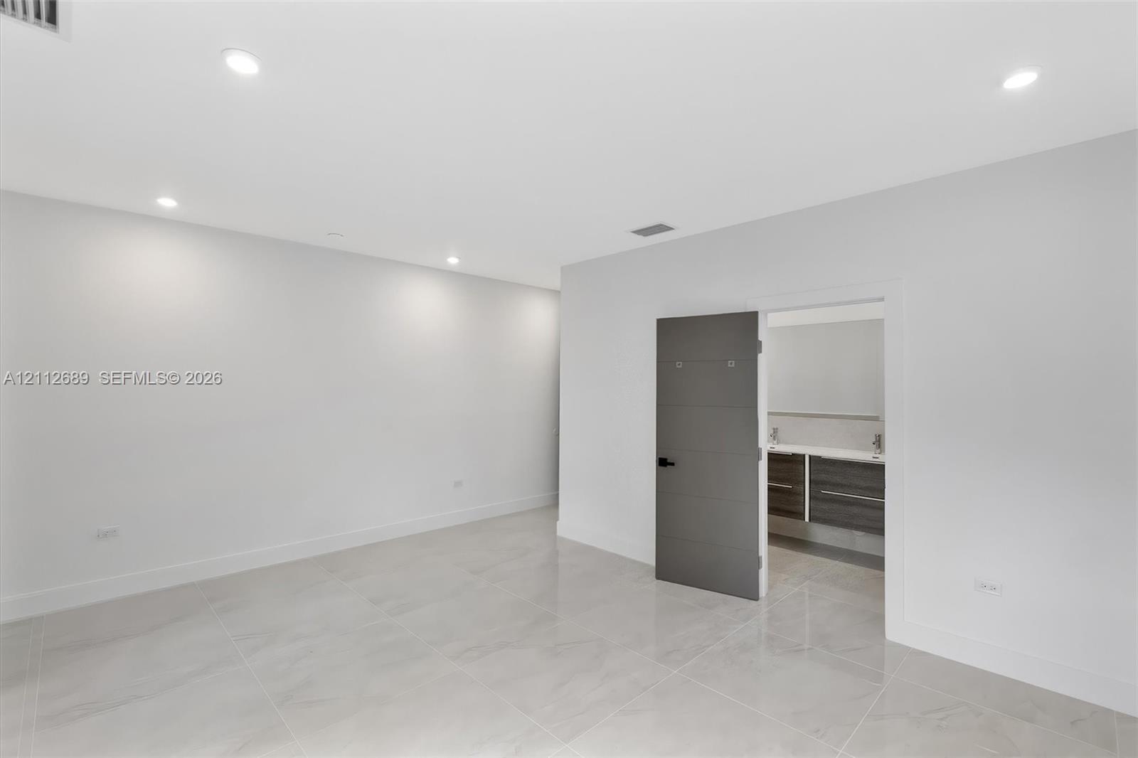 Neutral-toned large-format tile flooring, recessed ceiling lighting, and a modern slab-style interior door featuring horizontal accent grooves and mat
