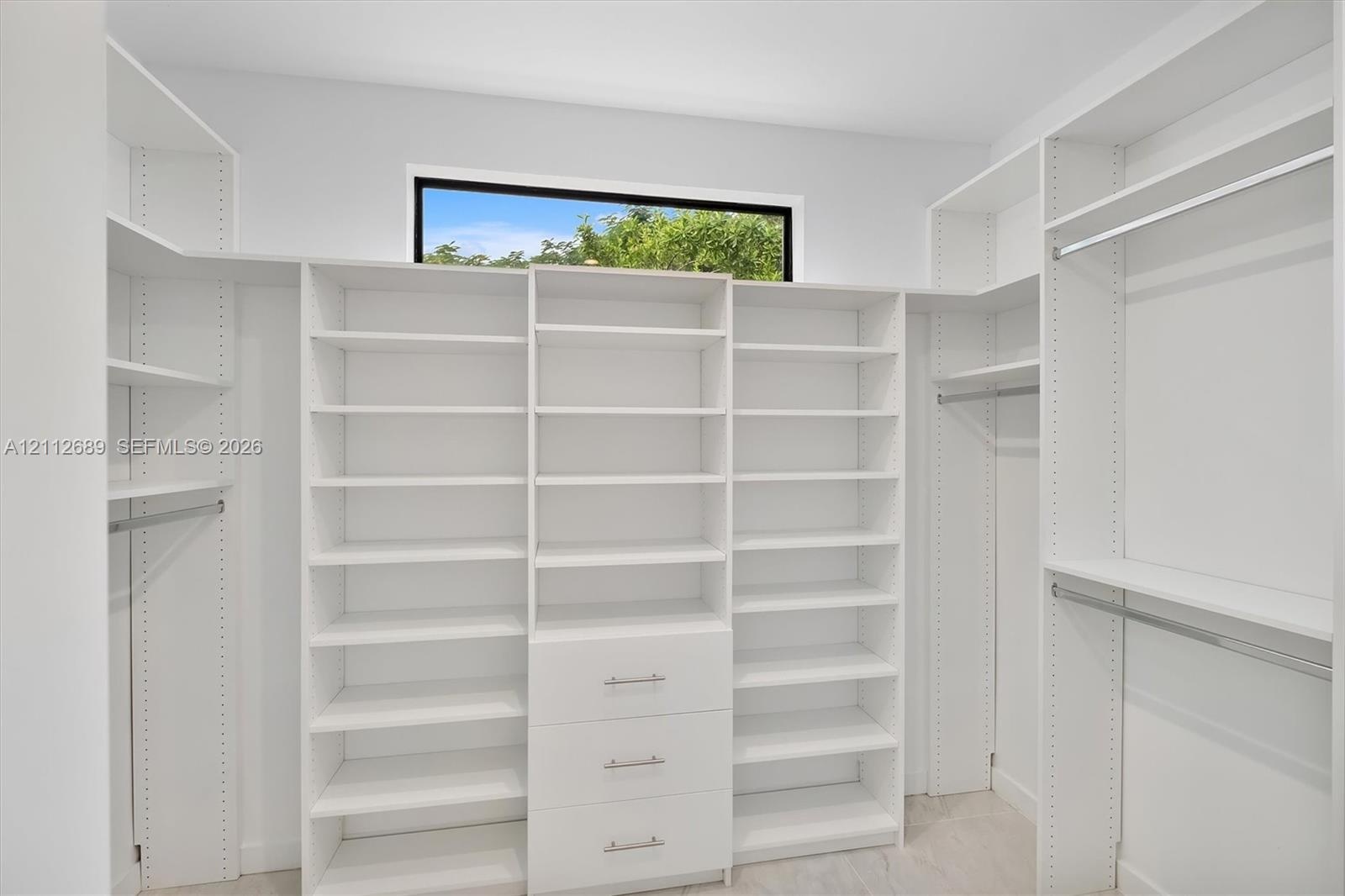 Walk-in closet featuring floor-to-ceiling white built-in shelving, integrated dresser drawers with metallic pulls, horizontal hanging rods, and a cler
