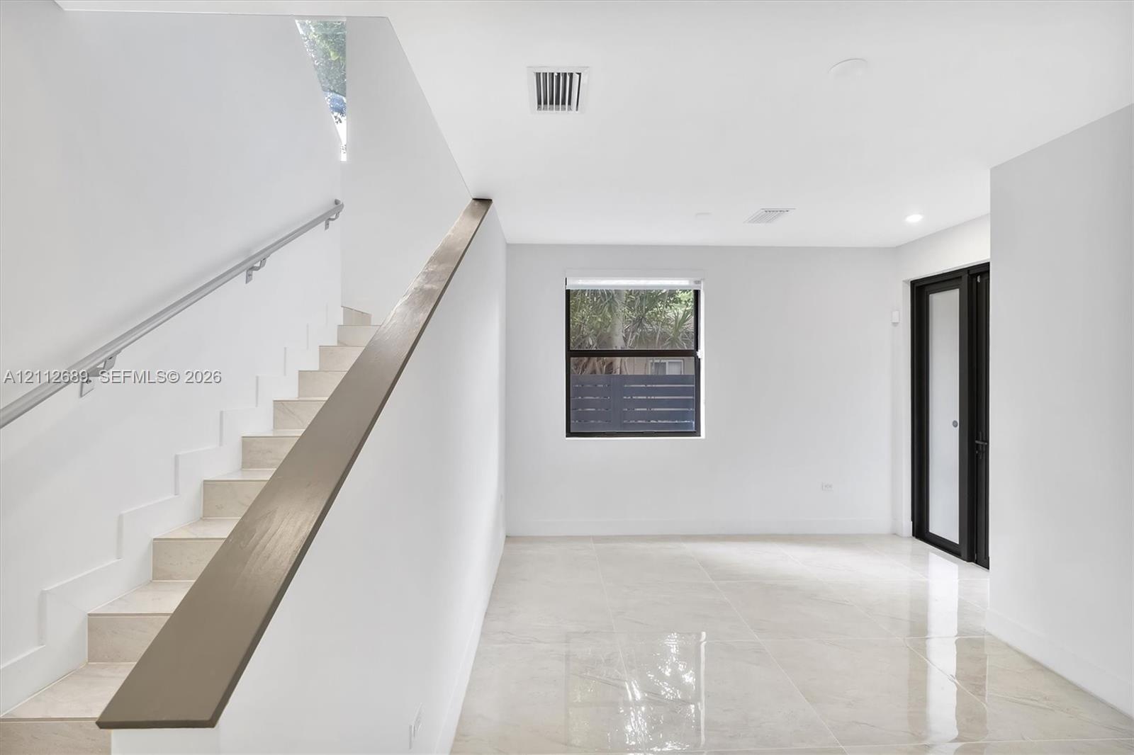 Interior space featuring polished tile flooring, a staircase with a minimalist metal handrail, a dark-finished accent banister, and a door with black 