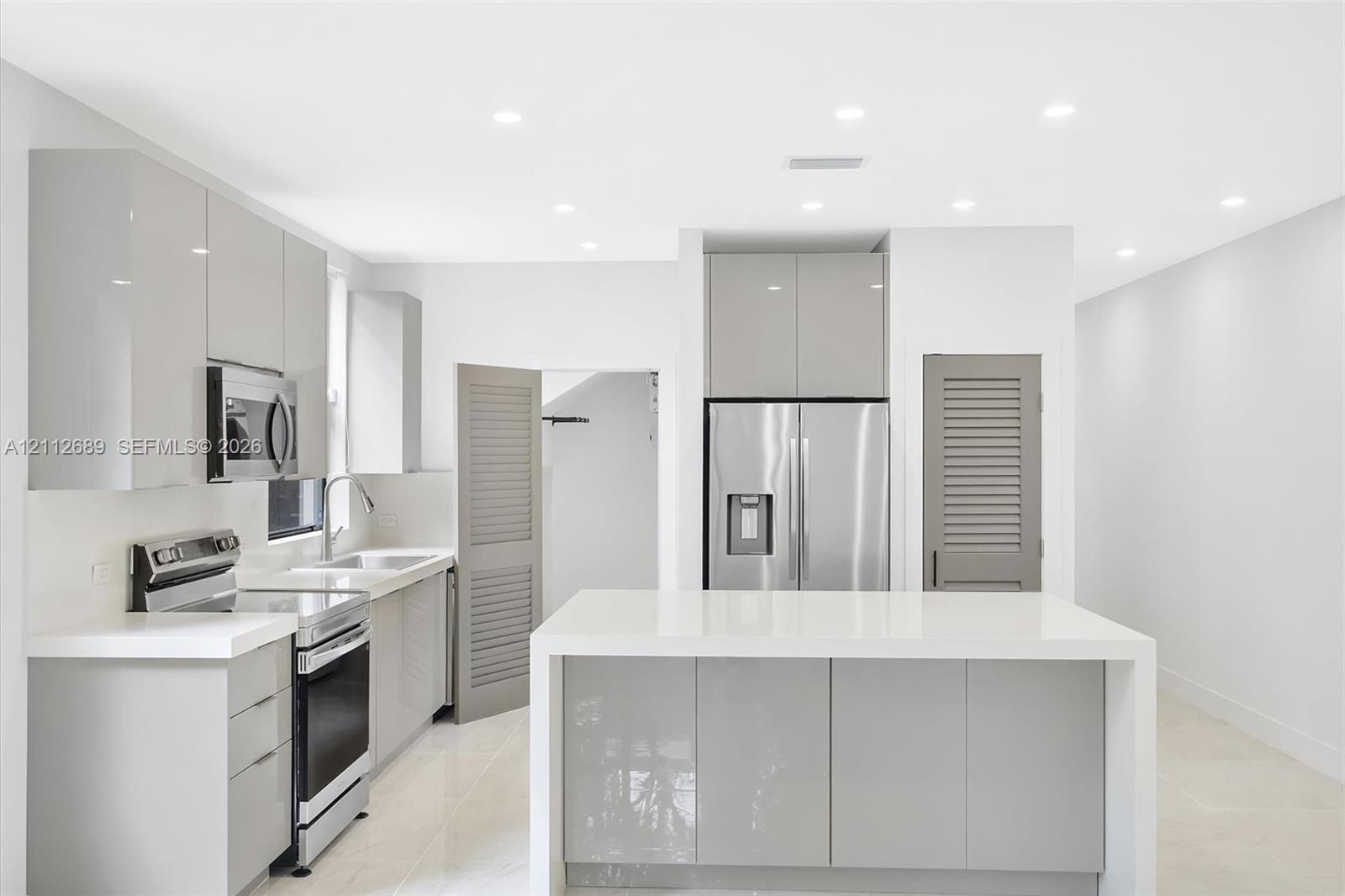 Contemporary kitchen featuring high-gloss cabinetry, a central island with a solid-surface countertop, stainless steel appliances, recessed ceiling li