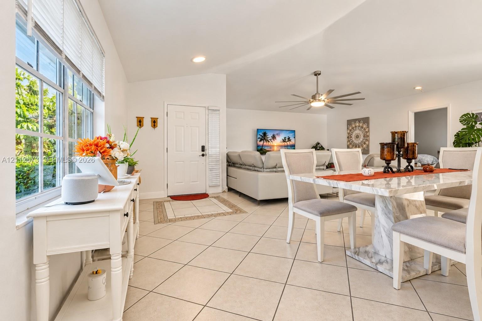 Open-concept area featuring vaulted ceilings, oversized grid-pattern windows, large-format tile flooring, and a multi-blade modern ceiling fan