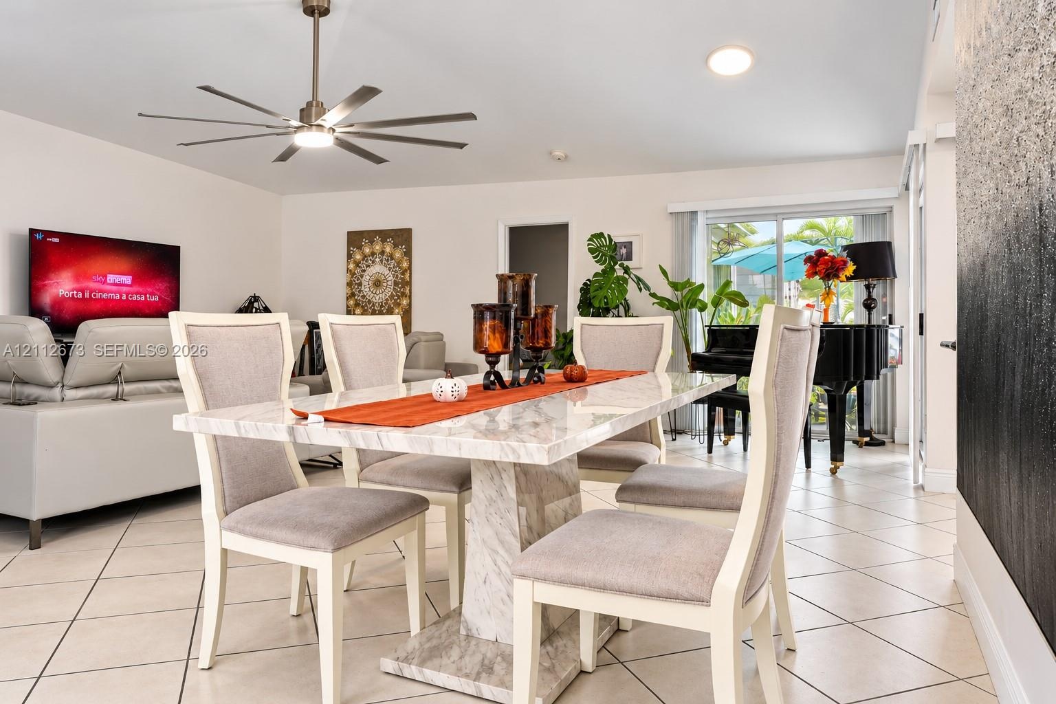 Open-concept interior featuring light-toned diagonal tile flooring, a multi-blade ceiling fan with integrated lighting, and glass sliding doors