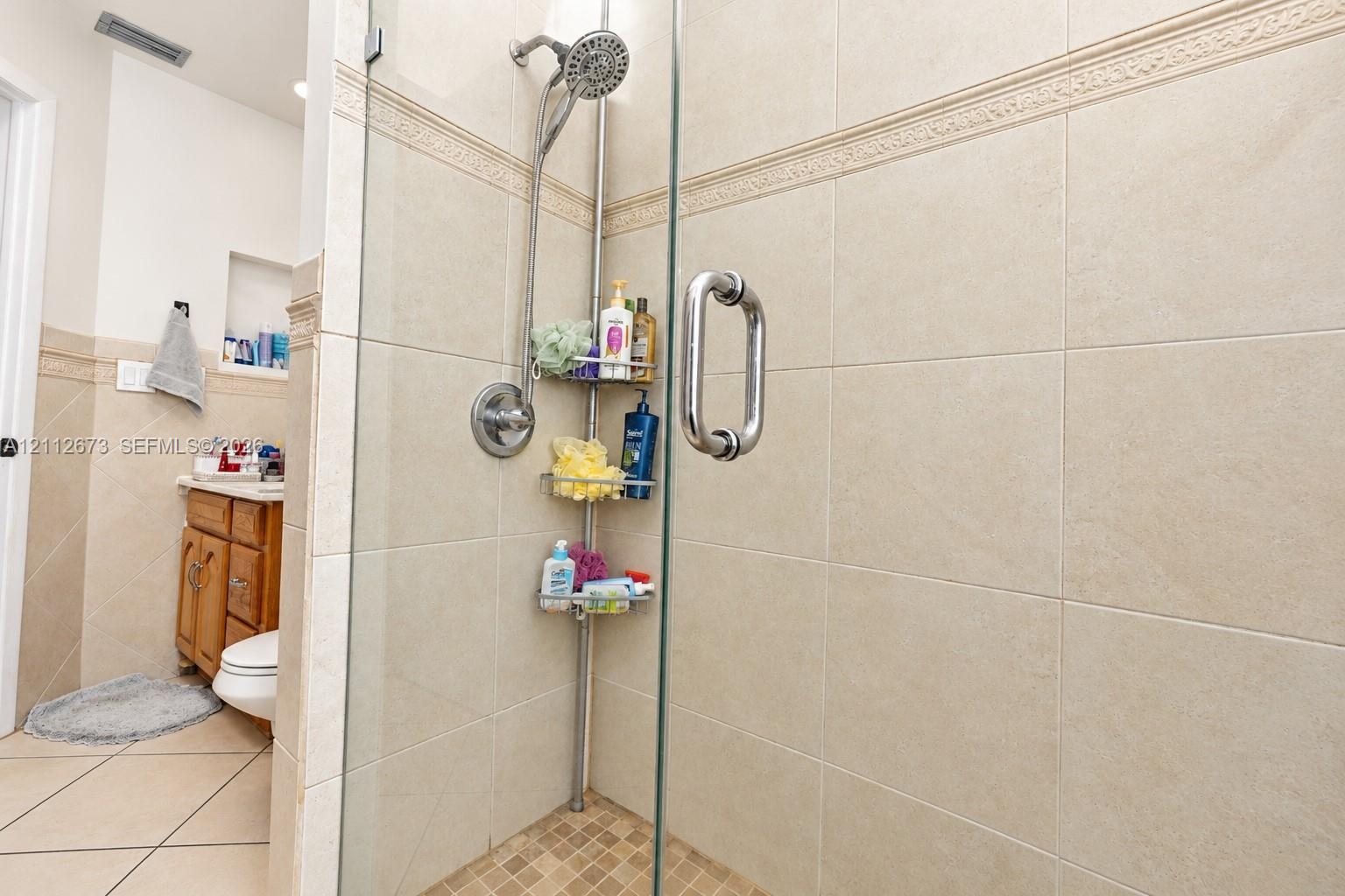 Walk-in shower featuring glass enclosure, large-format neutral wall tile, decorative tile accent band, and built-in wall niche