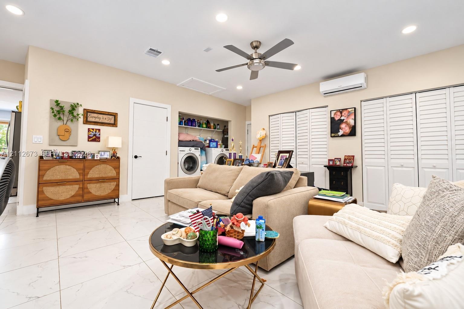 Large-format tile flooring, recessed ceiling lighting, brushed metal ceiling fan, wall-mounted ductless air conditioning unit, and white louvered bifo