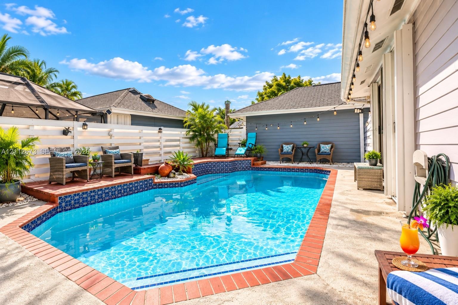 Outdoor swimming pool featuring decorative tile accents, a brick paver border, concrete patio, and white horizontal privacy fencing