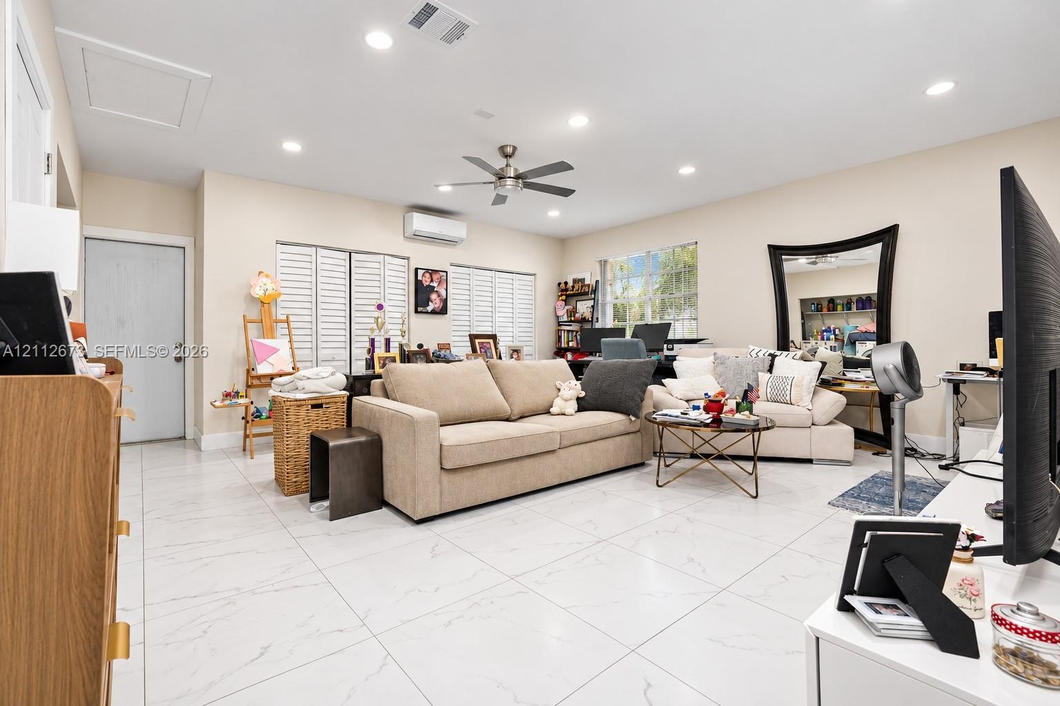 Living area featuring large-format tile flooring, recessed lighting, a ceiling fan, white louvered window shutters, and a wall-mounted ductless climat