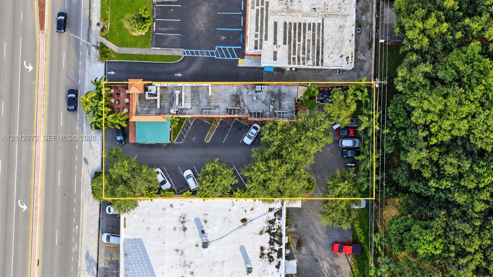 Aerial perspective of property featuring paved surface parking, mature perimeter trees, and street-front access