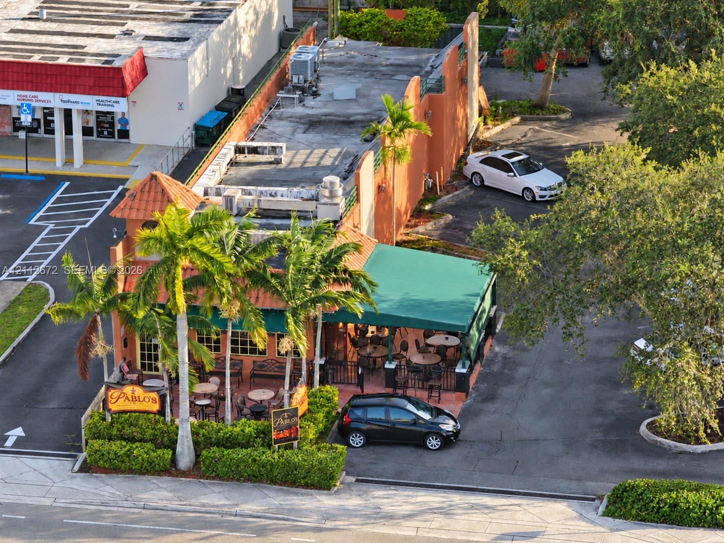 Commercial property featuring a stucco exterior, dedicated paved parking area, metal-frame outdoor canopy, and professional landscaping