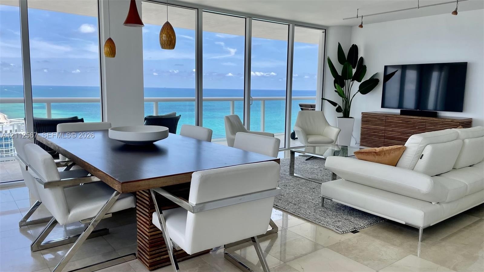 Open-concept living space featuring floor-to-ceiling glass walls, polished stone flooring, recessed track lighting, and a glass-railed balcony overloo