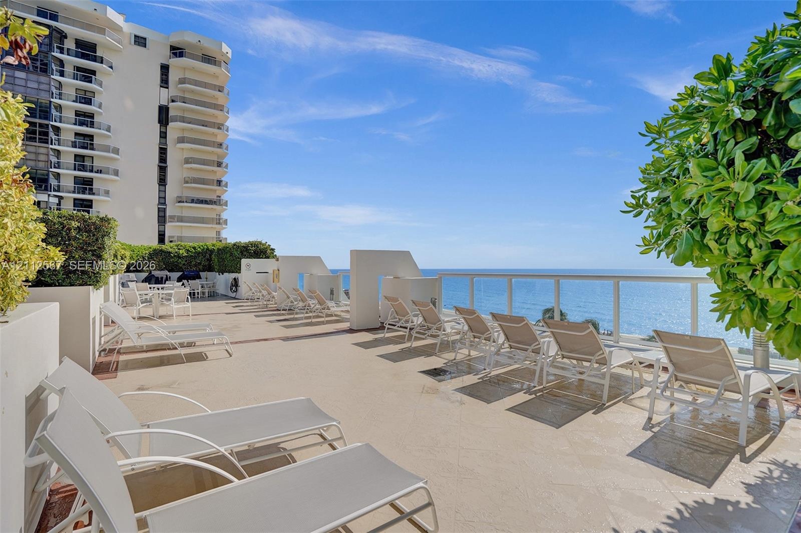 Expansive open-air terrace featuring stone-finish flooring, glass-paneled railings, and oceanfront placement