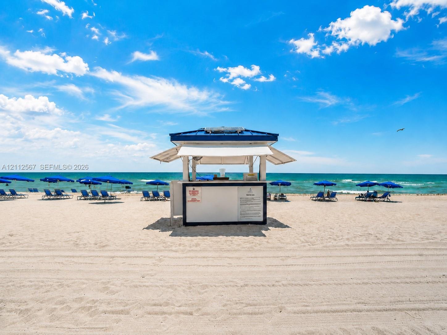 Standalone beachside kiosk featuring a blue metal roof, white facade, and an open service window