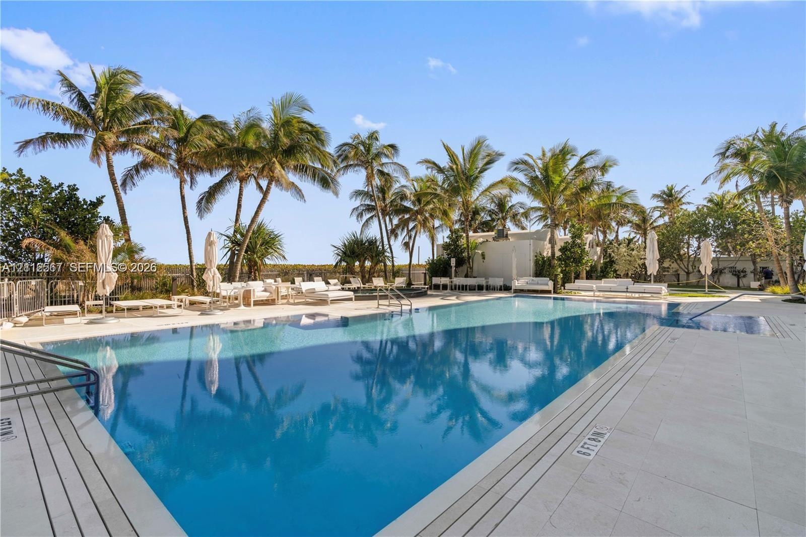 In-ground swimming pool featuring a tiled waterline, large stone-paver pool deck, integrated steps, and mature palm landscaping
