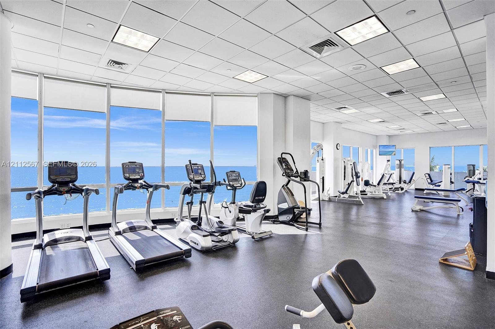 Fitness center featuring floor-to-ceiling windows, rubberized flooring, and recessed ceiling grid lighting