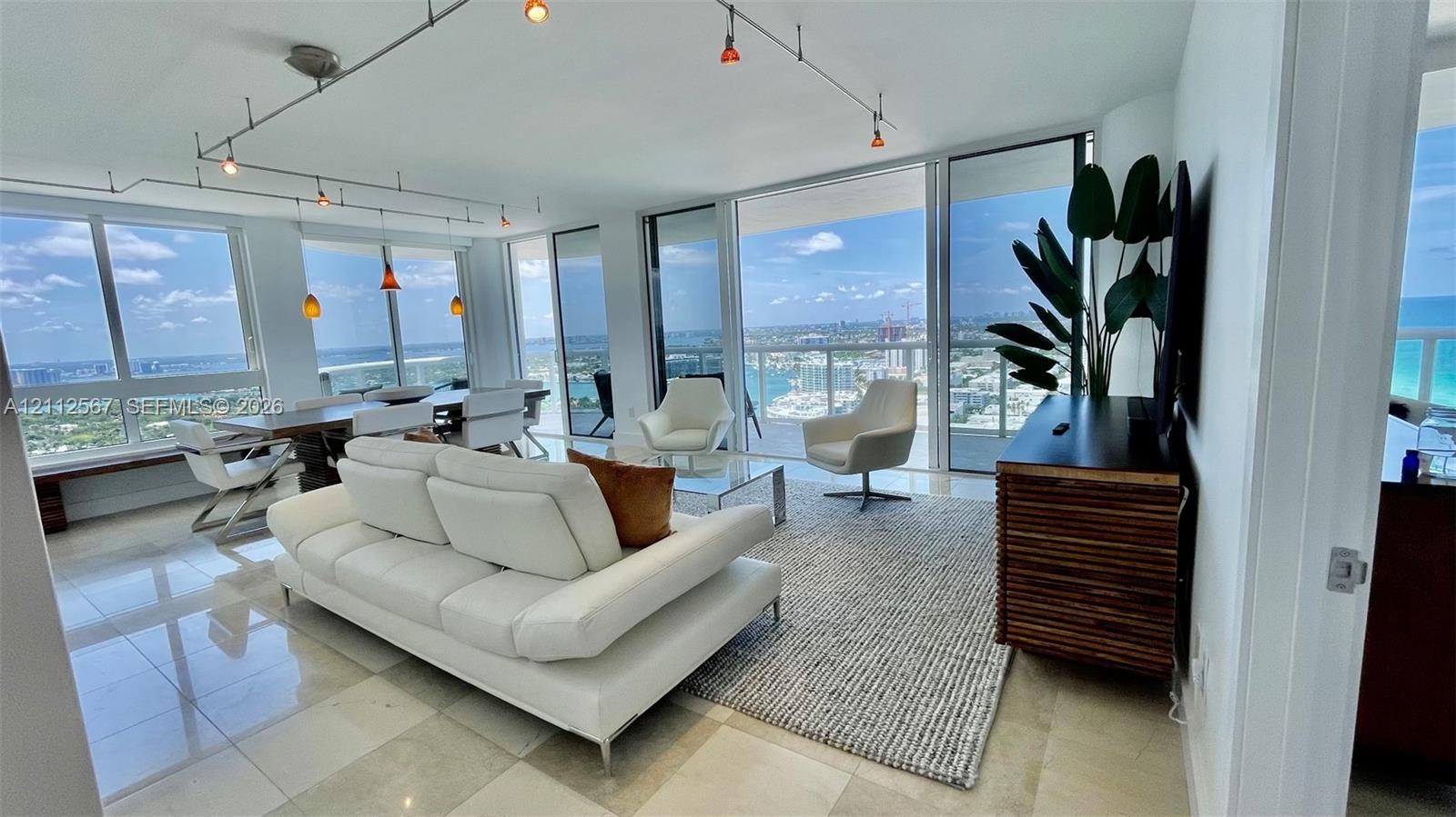 Living area featuring floor-to-ceiling glass walls, stone-finish tile flooring, and overhead track lighting