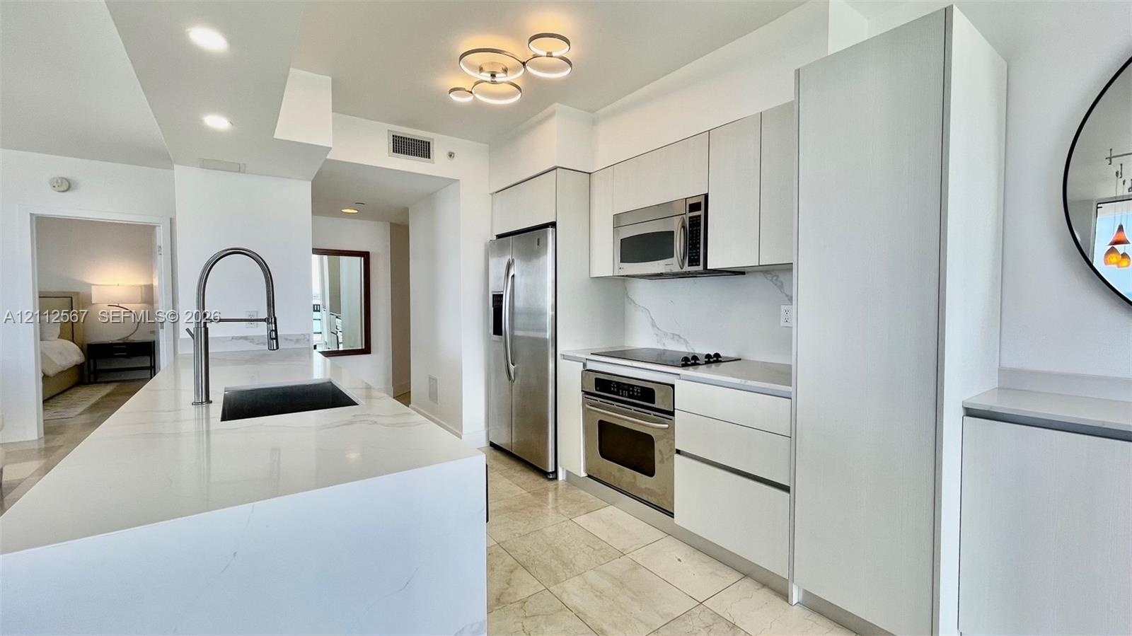 Kitchen featuring white flat-panel cabinetry, light-toned stone countertops, a waterfall-edge island, stainless steel appliances, and polished stone f
