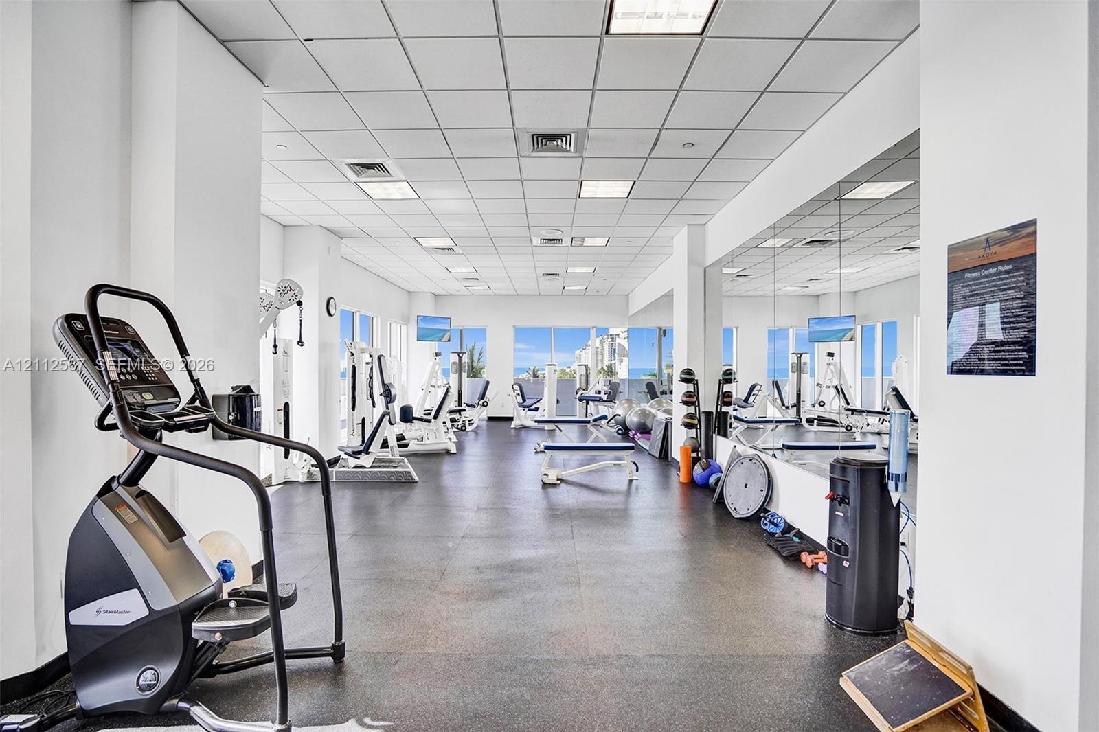 Fitness center featuring wall-to-wall mirrors, recessed grid ceiling lighting, impact-resistant rubber flooring, and large windows