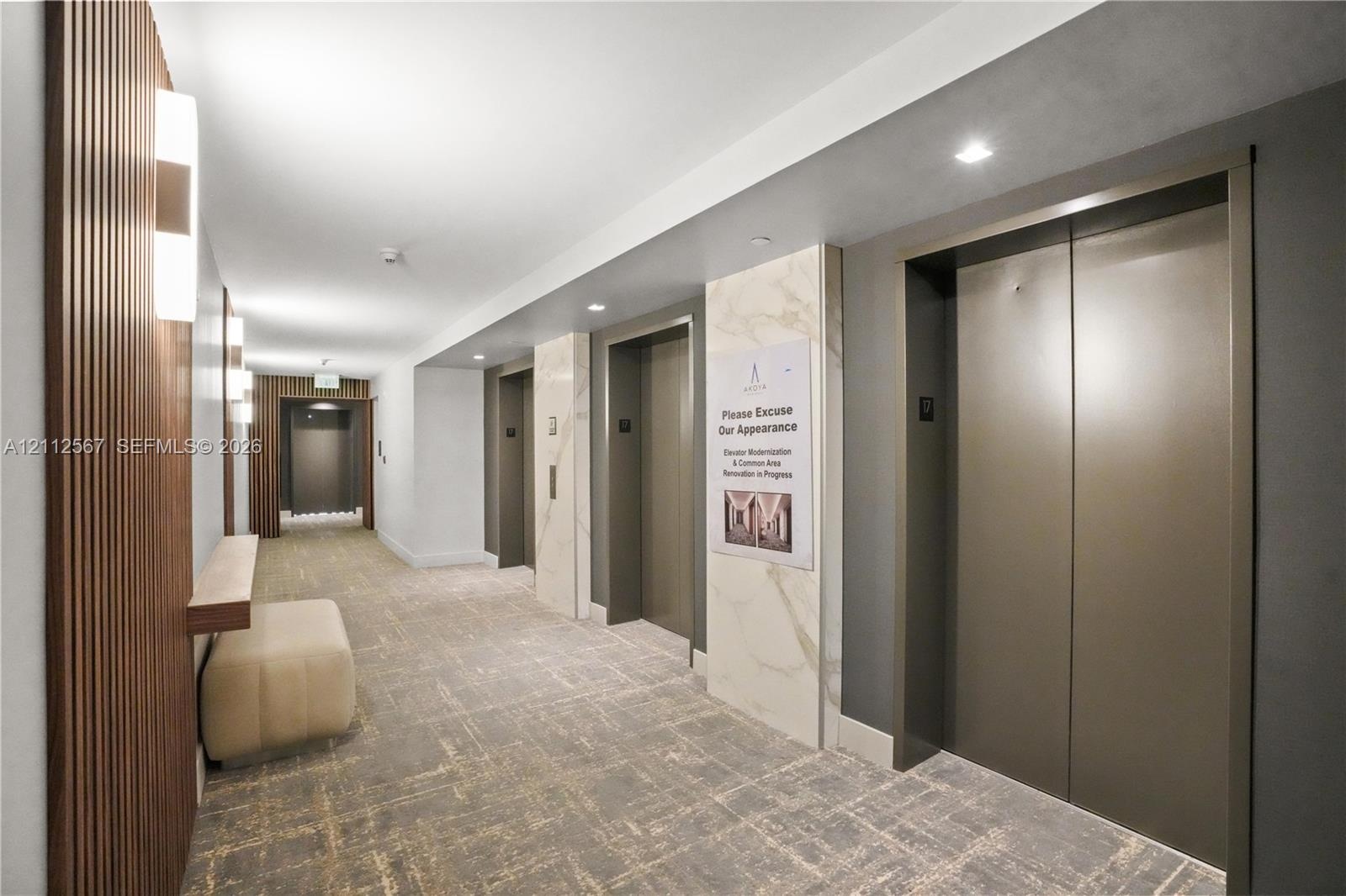 Common area featuring multi-panel elevator banks, vertical wood slat wall detailing, stone-clad pillar accents, recessed ceiling lighting, and wall-mo