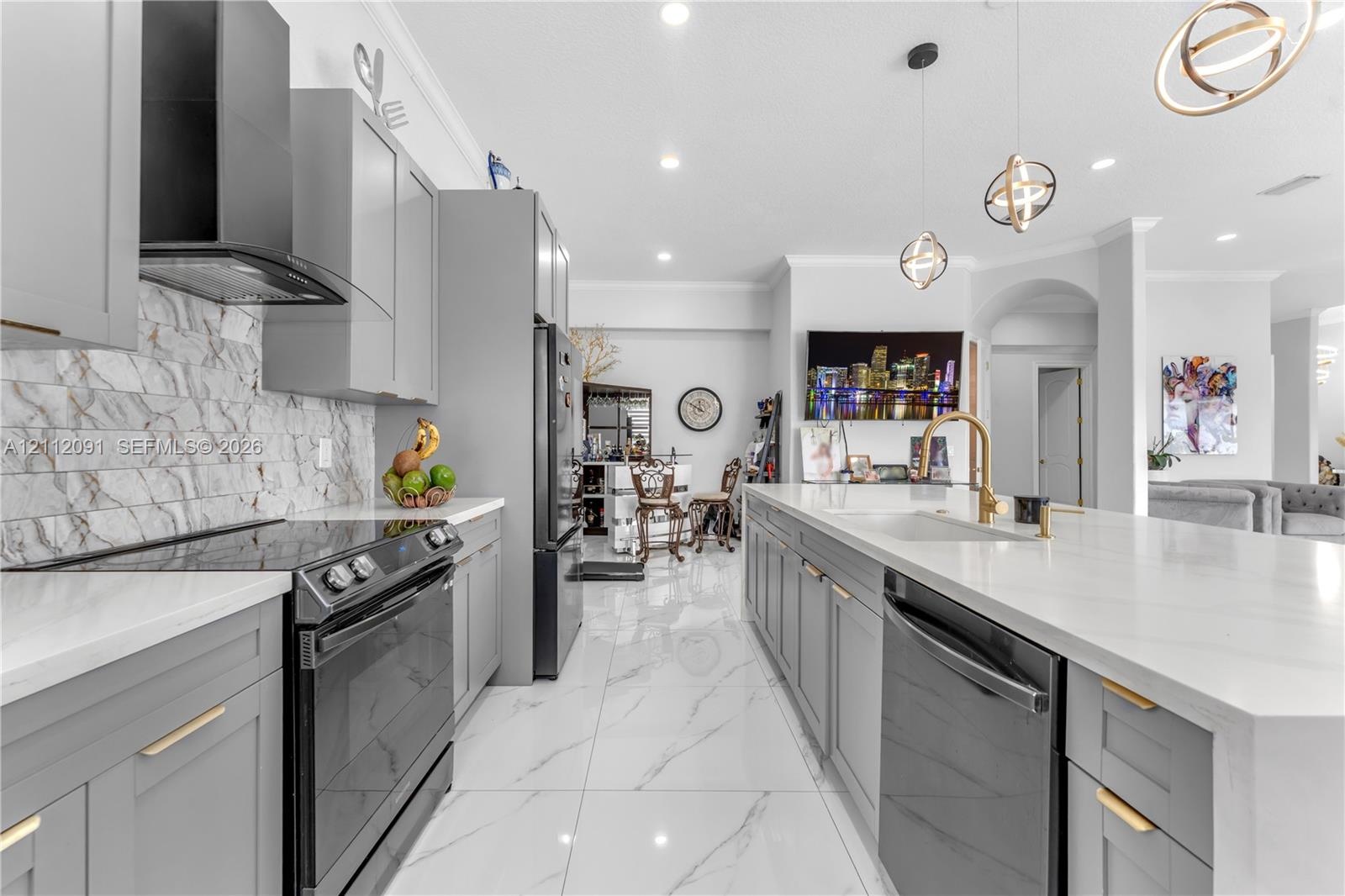 Kitchen featuring gray shaker-style cabinetry, a stone-pattern backsplash, quartz countertops, a central island with a gold-finish faucet, and large-f