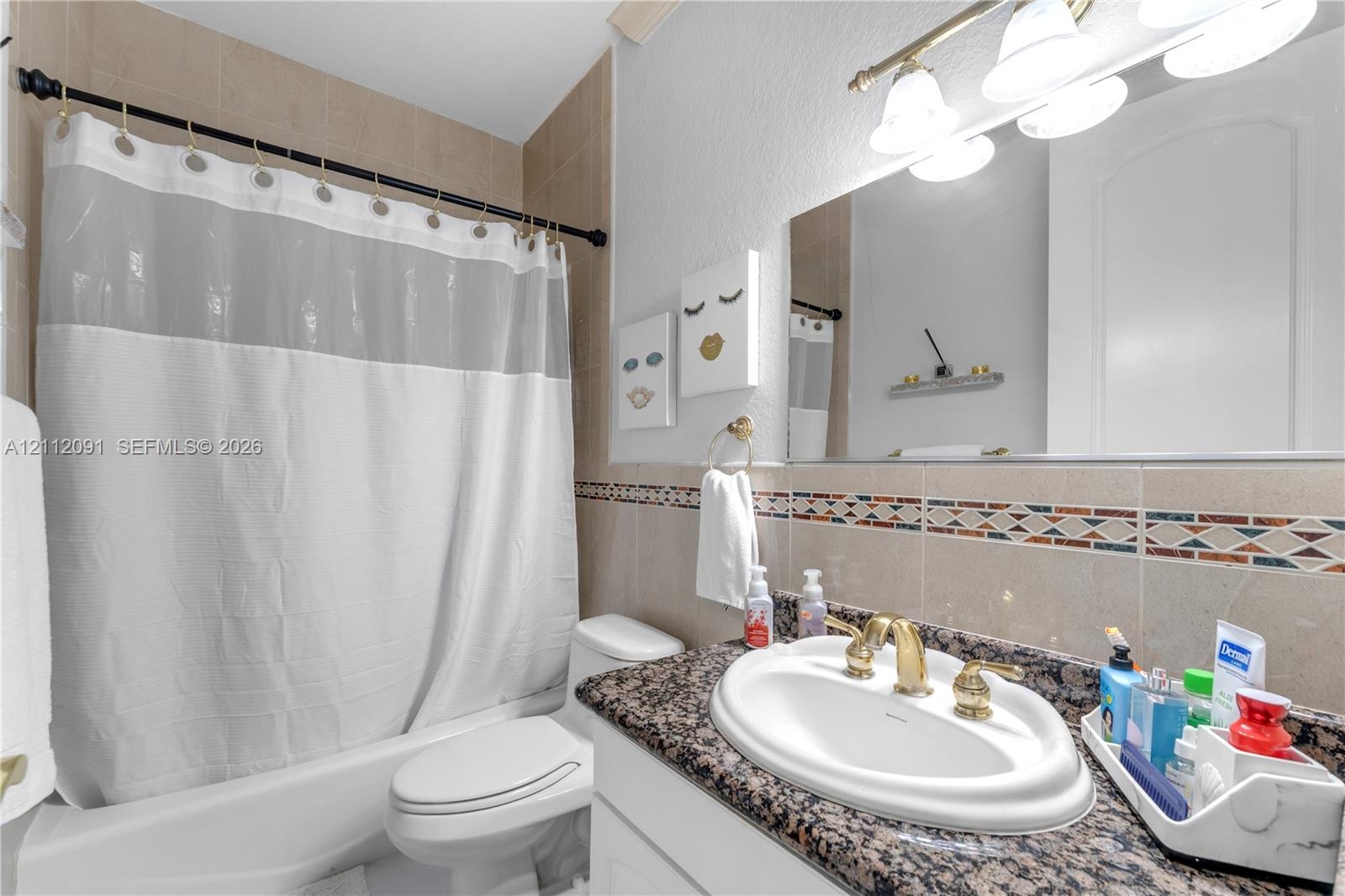 Bathroom featuring a stone-surface vanity countertop, drop-in sink with brass-toned hardware, decorative tile backsplash, and a tub-shower combination