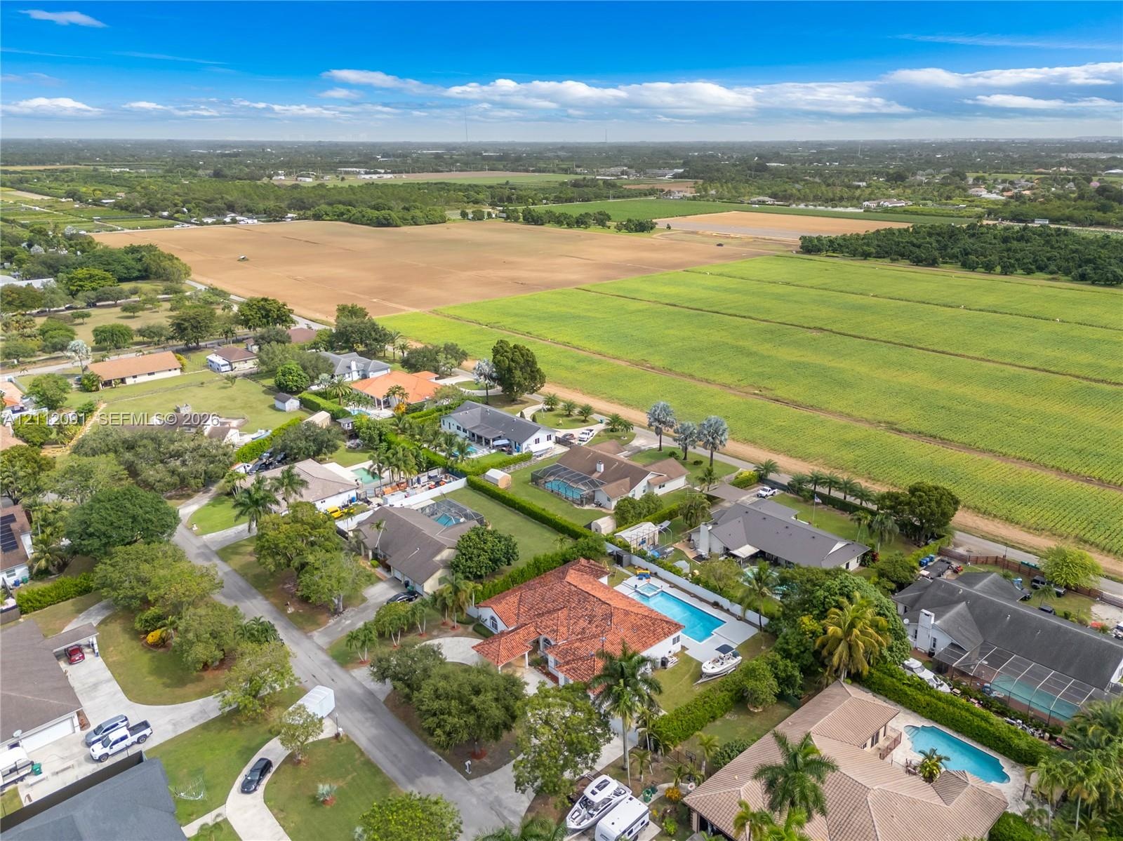 Aerial perspective of a sprawling residential property featuring a clay tile roof, a private swimming pool, concrete hardscaping, and mature palm tree