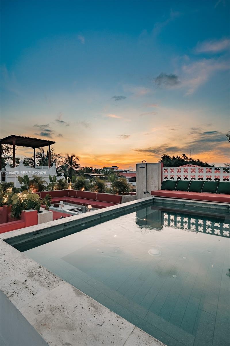 Rooftop terrace featuring a stone-lined pool, built-in masonry seating, a pergola, and decorative open-patterned privacy screening