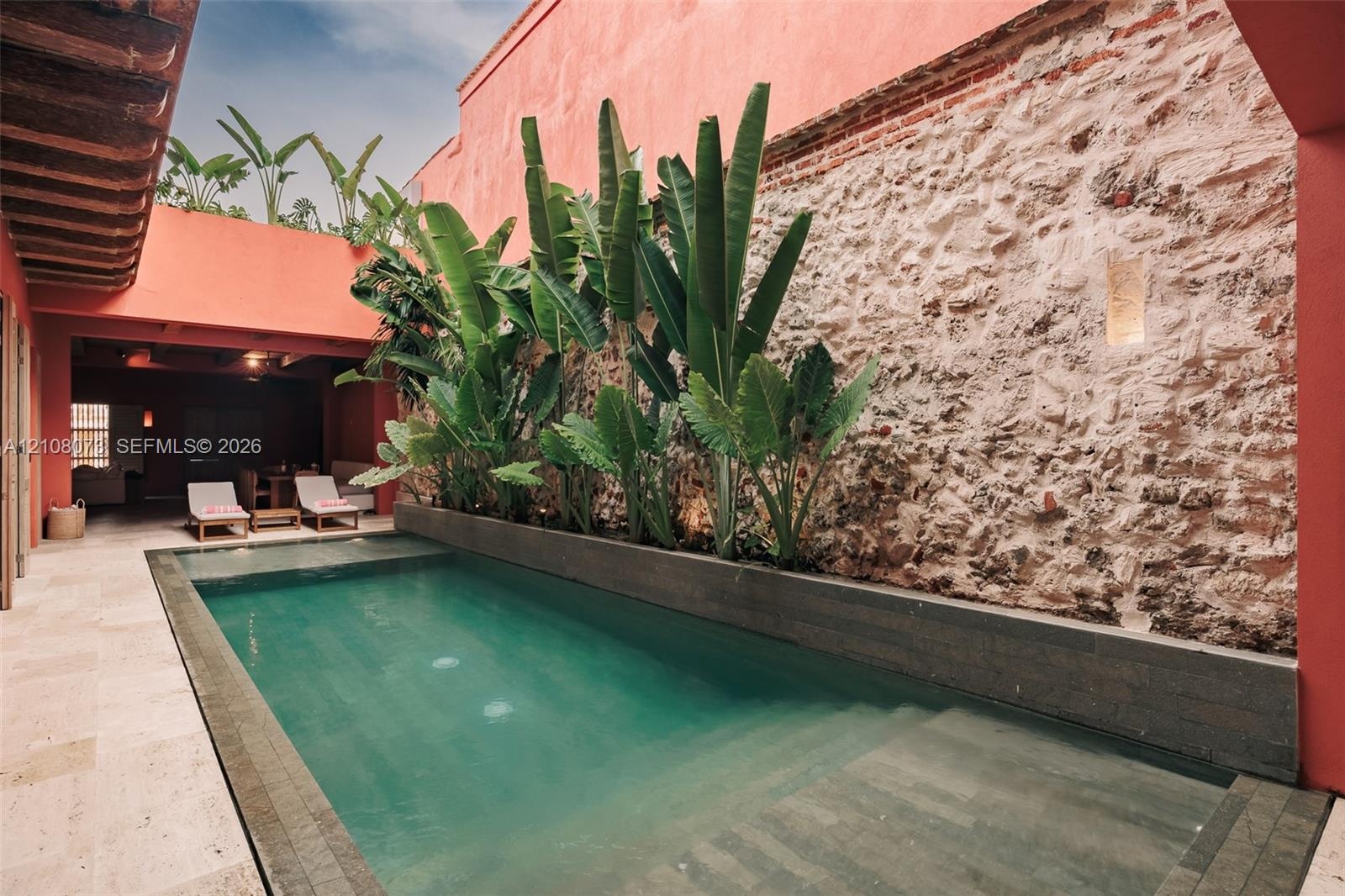 Courtyard pool featuring stone wall masonry, tile surround, integrated landscaping, and recessed wall lighting