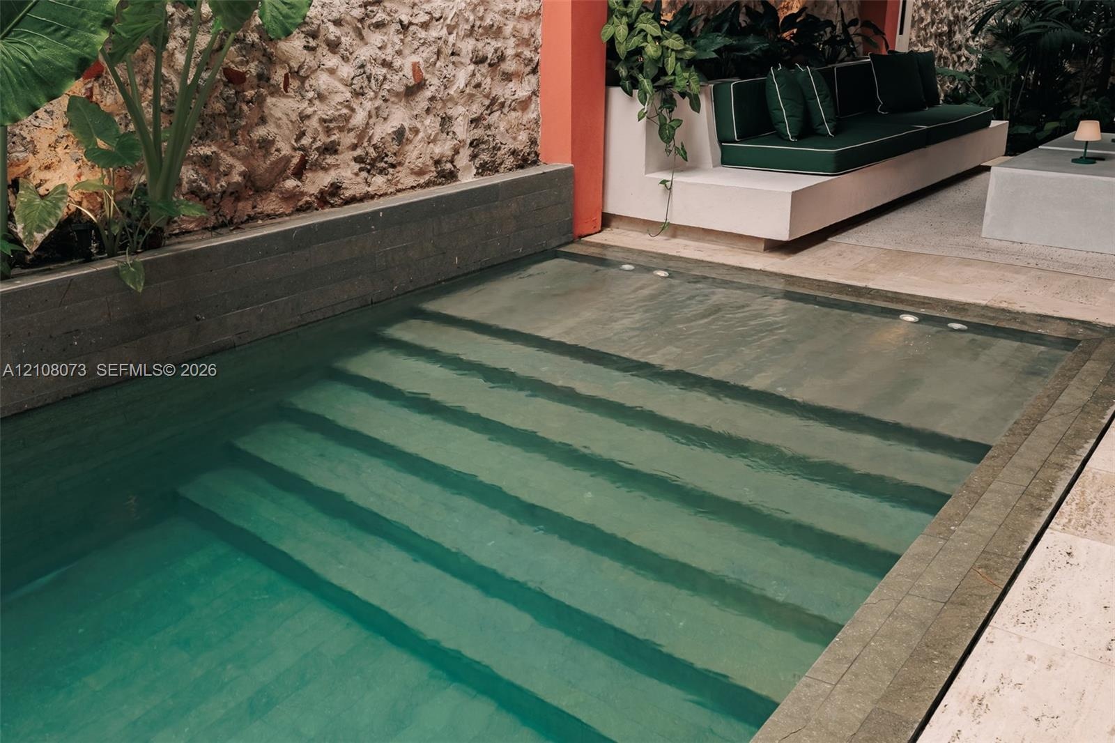 In-ground pool featuring integrated steps, natural stone wall, masonry tiered planter, and stone tile decking