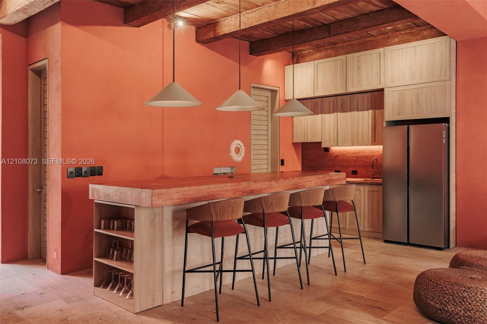 Kitchen featuring exposed wood ceiling beams, light-toned wood cabinetry, a central island with integrated shelving, and three cone-shaped pendant lig