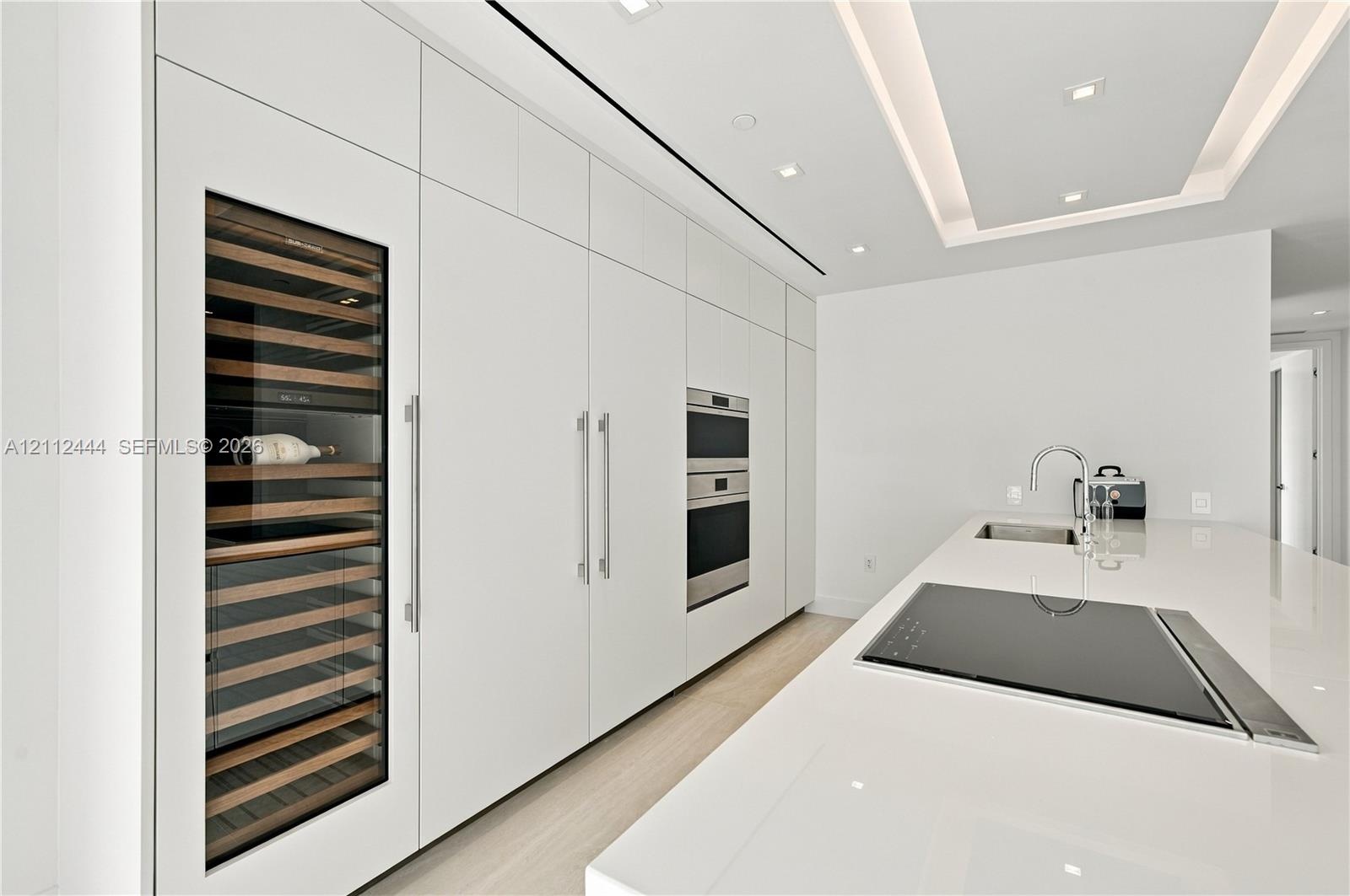 Sleek kitchen featuring custom floor-to-ceiling cabinetry, built-in stainless steel appliances, a glass-front wine refrigerator, and a solid-surface i