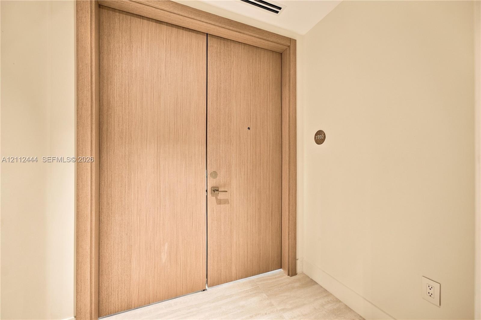 Double-door entry featuring light wood-finish slab doors with matching door casing and metallic hardware