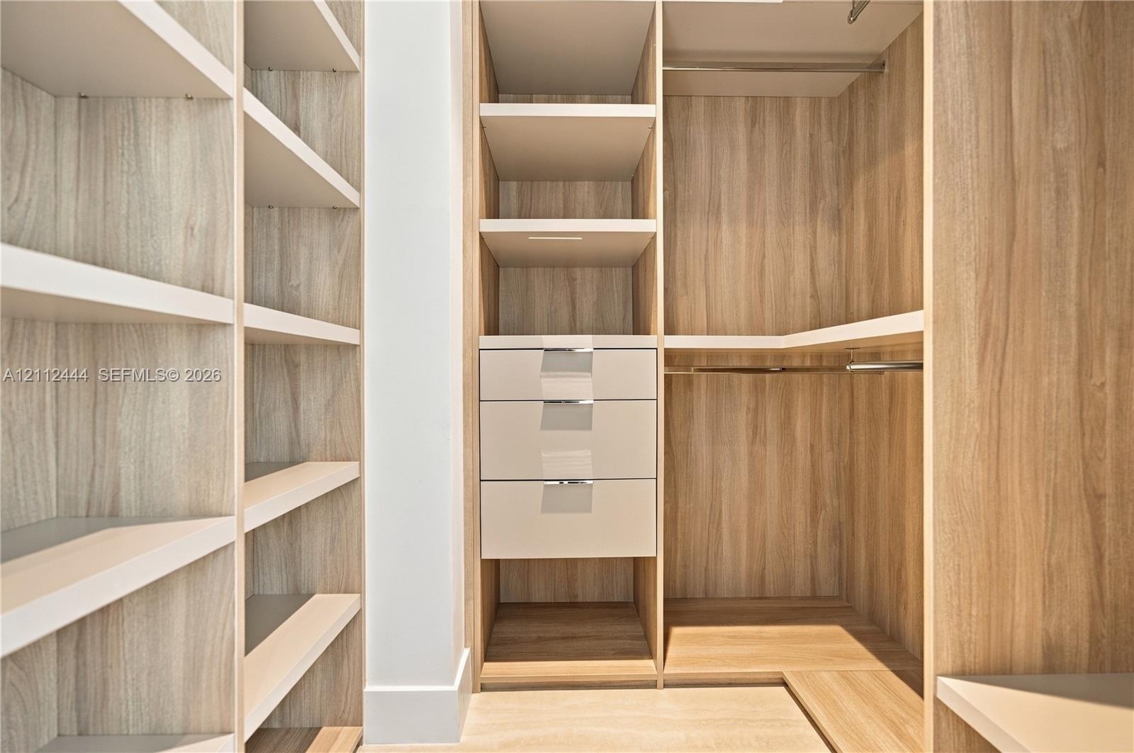 Custom walk-in closet featuring wood-finish cabinetry, built-in shelving, integrated drawers with metal pulls, and polished metal hanging rods