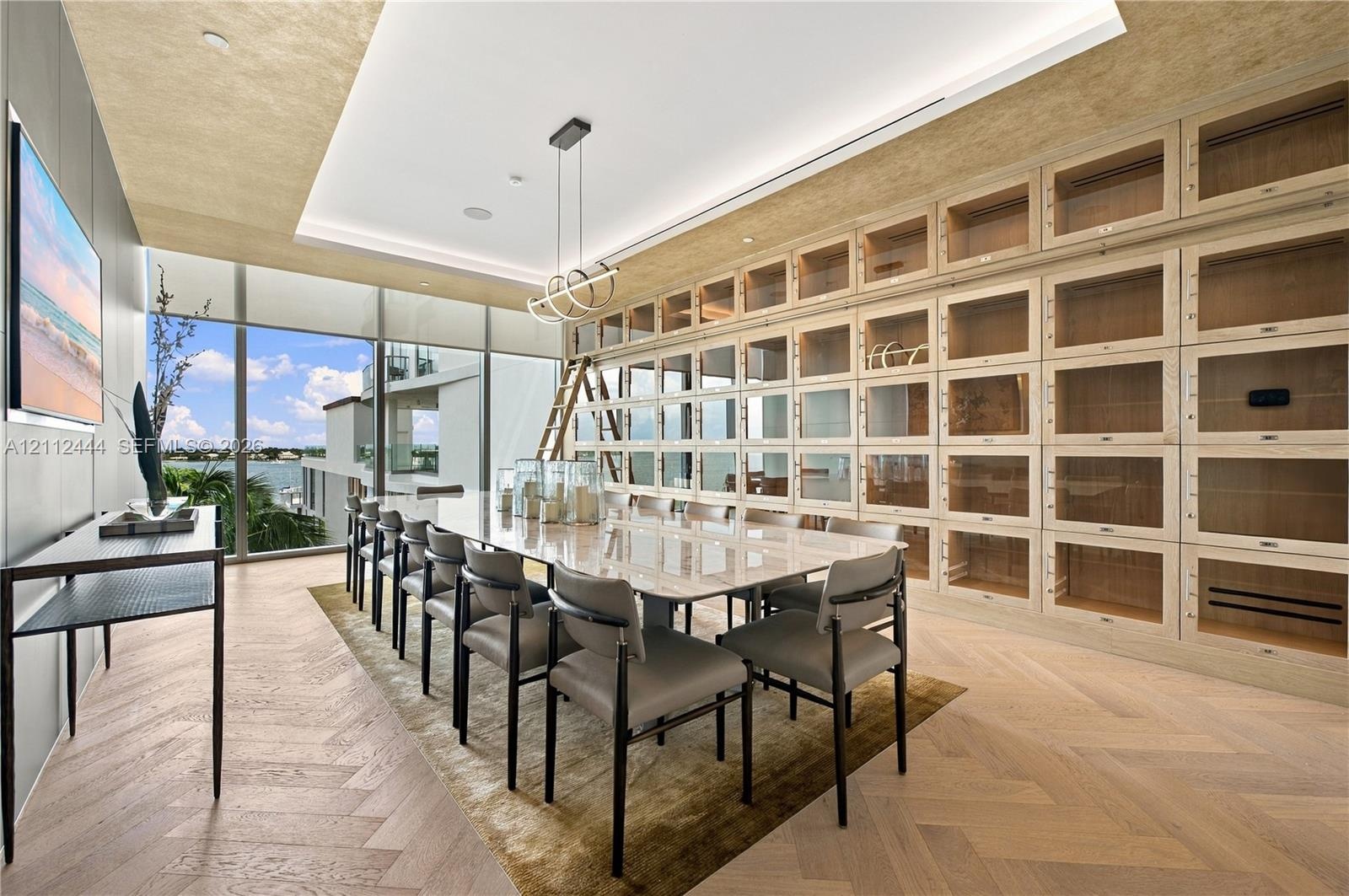 Floor-to-ceiling built-in cabinetry with integrated rolling library ladder, wood-finish herringbone flooring, recessed tray ceiling, modern linear pen