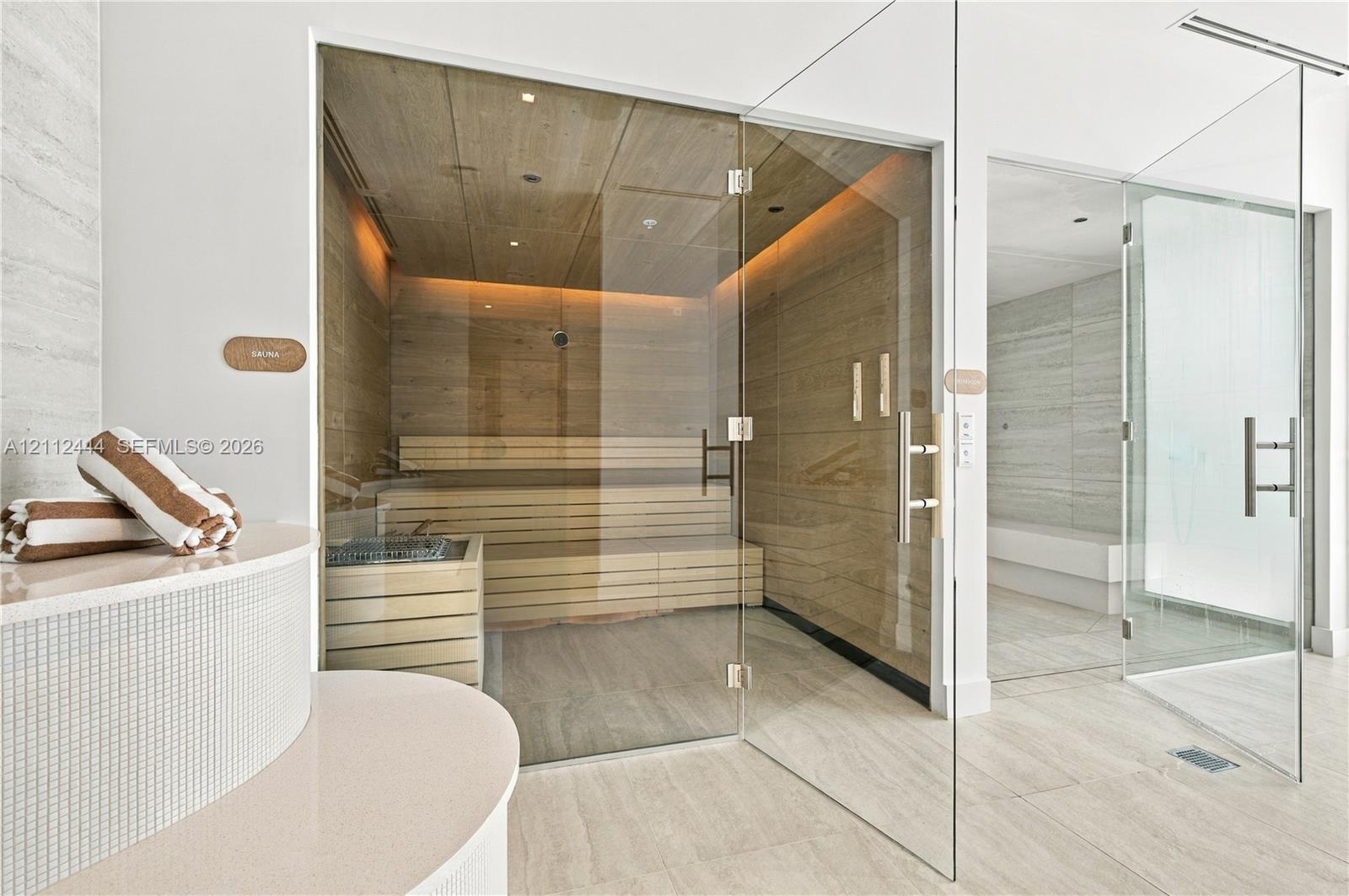 Custom sauna featuring wood-panelled interior, multi-level bench seating, and glass enclosure, paired with a glass-enclosed steam shower featuring neu
